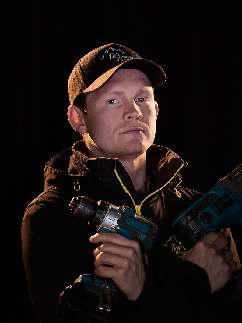 Mann med caps og svart jakke, med verktøy i hendene.